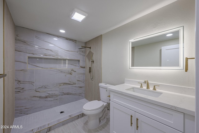 bathroom with a tile shower, vanity, and toilet