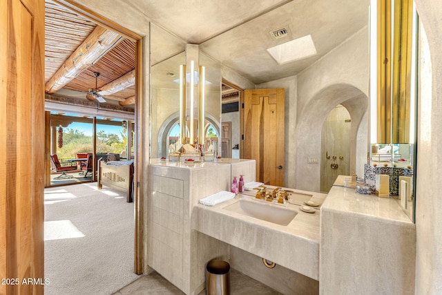 bathroom with ceiling fan, sink, beam ceiling, and a skylight