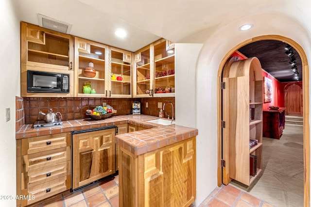 bar featuring black microwave, sink, tile counters, and decorative backsplash