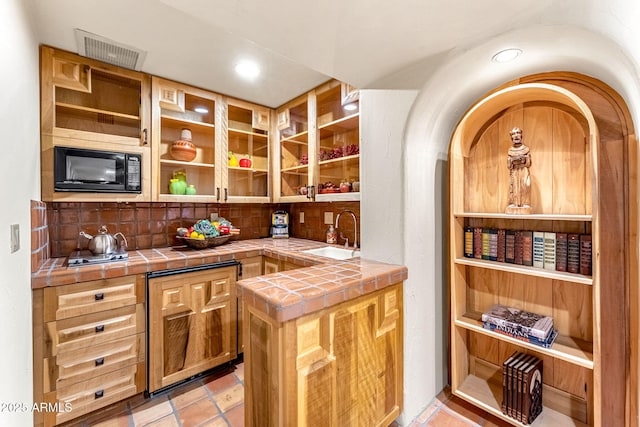 interior space with sink, tile countertops, black microwave, kitchen peninsula, and backsplash