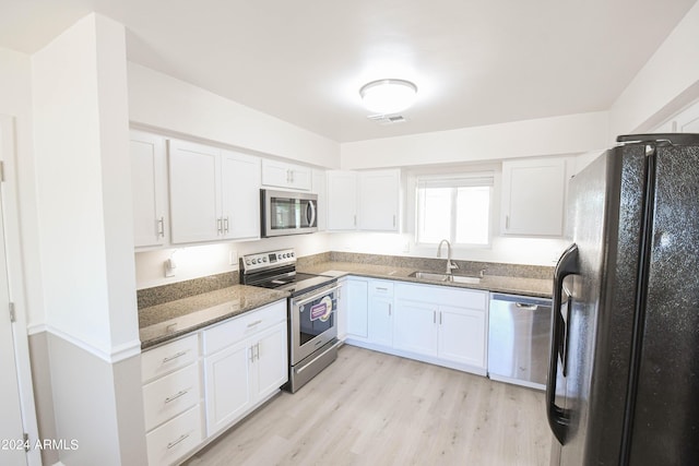 kitchen with sink, light hardwood / wood-style flooring, appliances with stainless steel finishes, dark stone countertops, and white cabinets