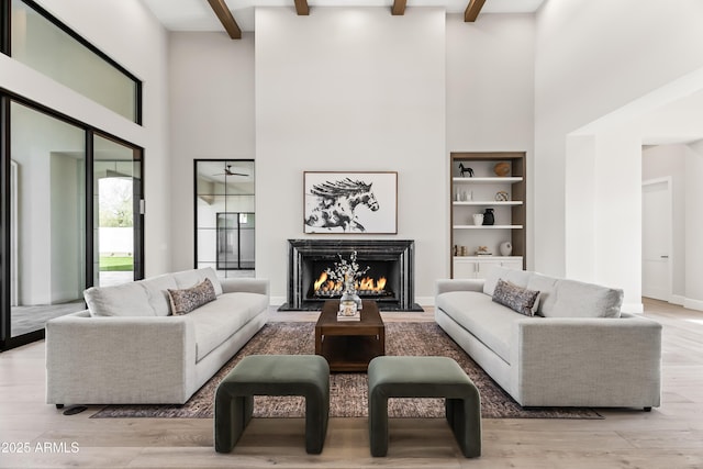 living area featuring beamed ceiling, a lit fireplace, wood finished floors, and a towering ceiling