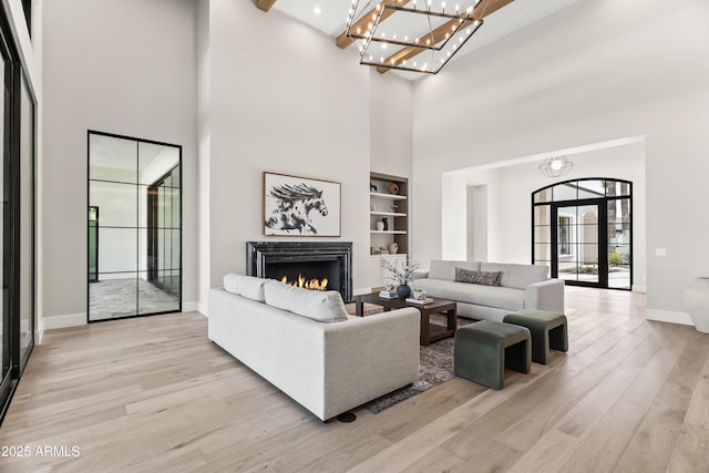 living room with a notable chandelier, built in features, beamed ceiling, and light wood-type flooring