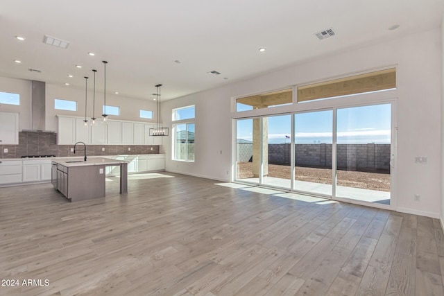 kitchen with a center island with sink, sink, wall chimney exhaust hood, decorative light fixtures, and white cabinets