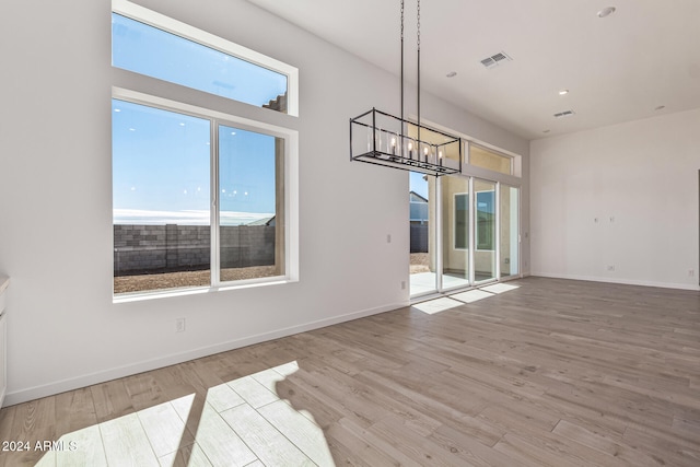 unfurnished dining area with light wood-type flooring, a healthy amount of sunlight, and a chandelier