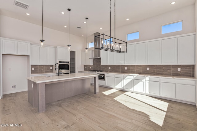 kitchen with a towering ceiling, appliances with stainless steel finishes, a center island with sink, and light hardwood / wood-style flooring