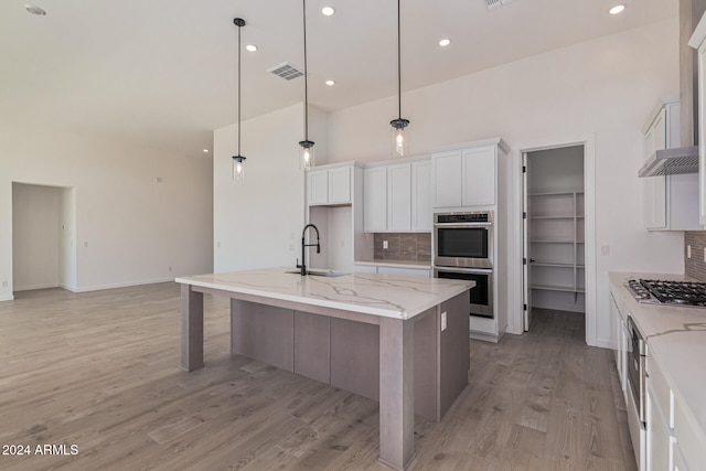 kitchen featuring stainless steel appliances, white cabinetry, a kitchen island with sink, pendant lighting, and decorative backsplash