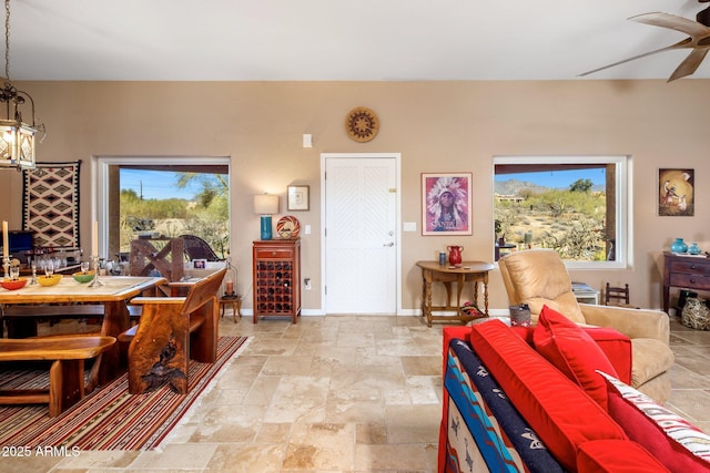 dining room with stone finish flooring, baseboards, a healthy amount of sunlight, and ceiling fan with notable chandelier