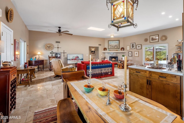 dining room featuring recessed lighting, a warm lit fireplace, stone tile flooring, and a ceiling fan