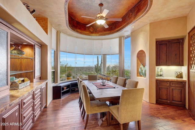 dining area with a raised ceiling, a high ceiling, dark hardwood / wood-style floors, and ceiling fan