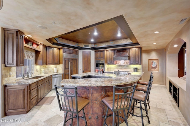 kitchen featuring light stone counters, custom range hood, stainless steel appliances, and a raised ceiling