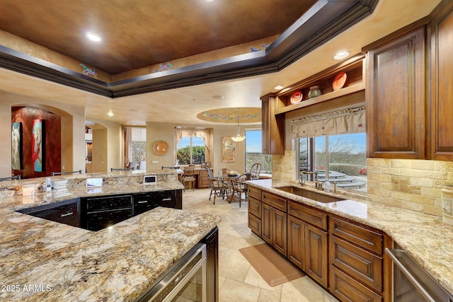 kitchen with crown molding, backsplash, light stone counters, decorative light fixtures, and a raised ceiling