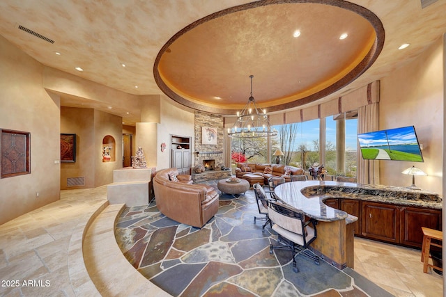 living room with a notable chandelier, a fireplace, a raised ceiling, and a high ceiling