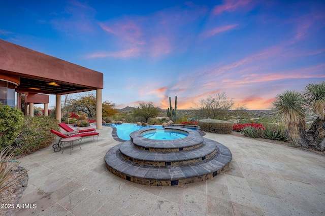 patio terrace at dusk featuring a swimming pool with hot tub