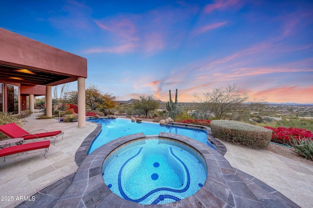 pool at dusk featuring an in ground hot tub and a patio