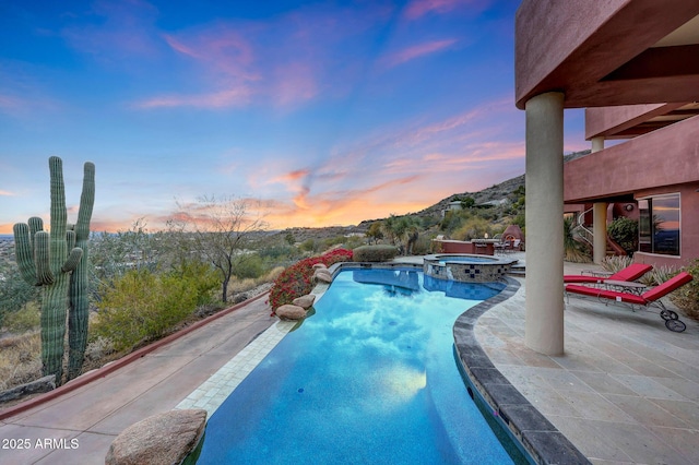 pool at dusk featuring an in ground hot tub, a mountain view, and a patio area