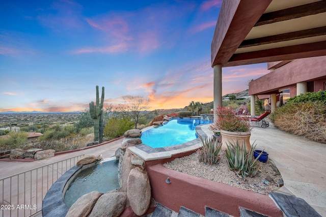 pool at dusk featuring a hot tub and a patio area