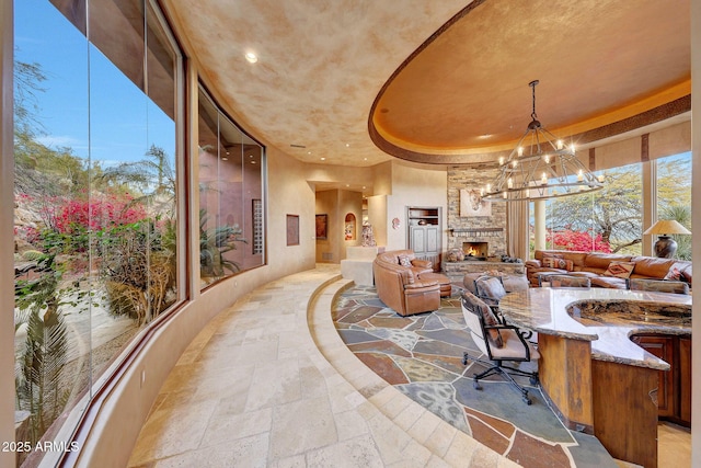 dining space featuring a raised ceiling, a stone fireplace, and a notable chandelier