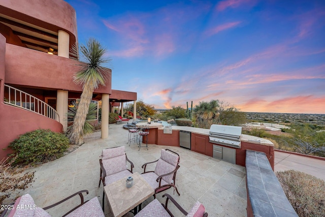 patio terrace at dusk featuring a grill and exterior kitchen