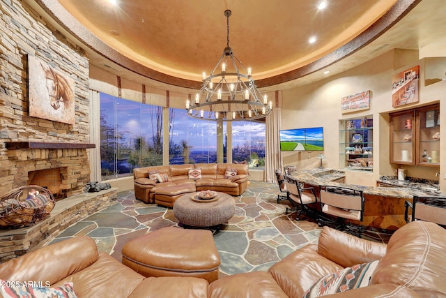 living room with a raised ceiling, a stone fireplace, and a notable chandelier