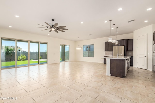 kitchen with pendant lighting, stainless steel refrigerator, a kitchen island with sink, ceiling fan, and dark brown cabinets