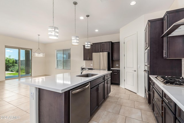 kitchen featuring decorative light fixtures, sink, dark brown cabinetry, stainless steel appliances, and a center island with sink