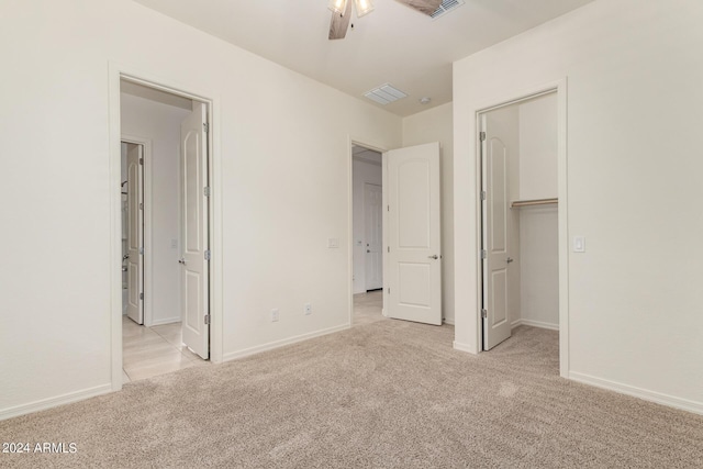 unfurnished bedroom featuring ceiling fan, light colored carpet, a closet, and a walk in closet