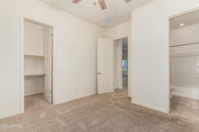 unfurnished bedroom featuring connected bathroom, a walk in closet, light colored carpet, a closet, and ceiling fan