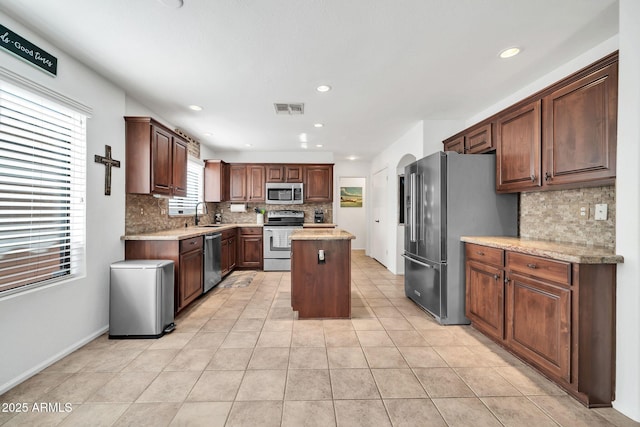 kitchen with decorative backsplash, appliances with stainless steel finishes, sink, light tile patterned floors, and a center island