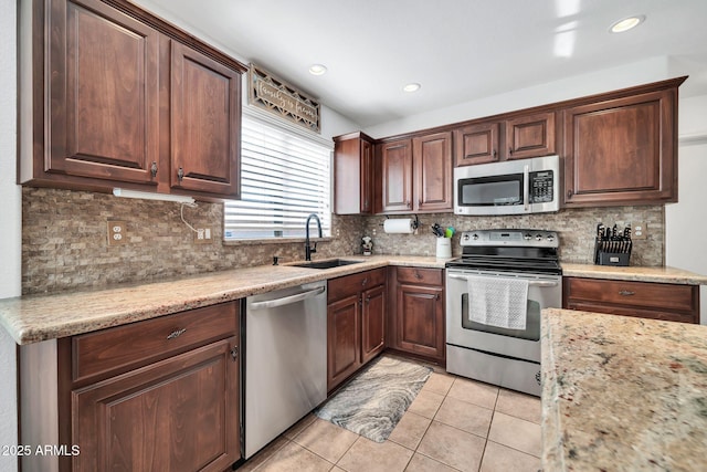 kitchen with appliances with stainless steel finishes, backsplash, light stone counters, sink, and light tile patterned flooring