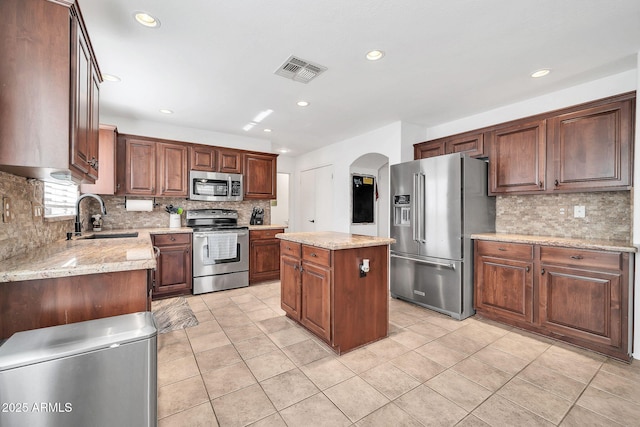 kitchen with light stone counters, stainless steel appliances, a kitchen island, and sink