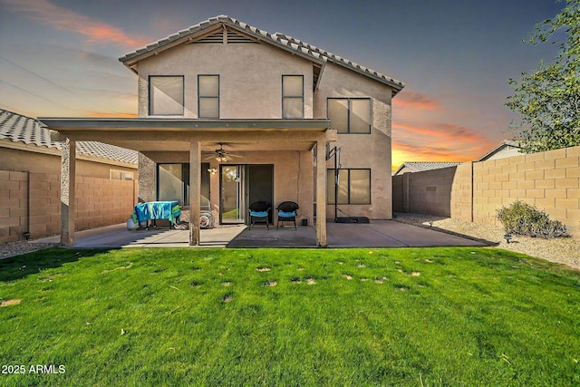 back house at dusk with a lawn, ceiling fan, and a patio