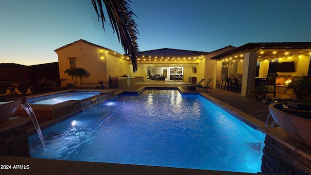 pool at dusk with an in ground hot tub, pool water feature, and a patio area