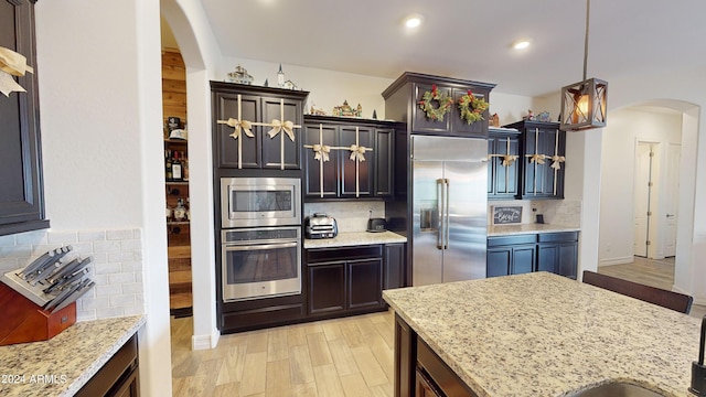 kitchen featuring light stone counters, backsplash, built in appliances, decorative light fixtures, and light wood-type flooring