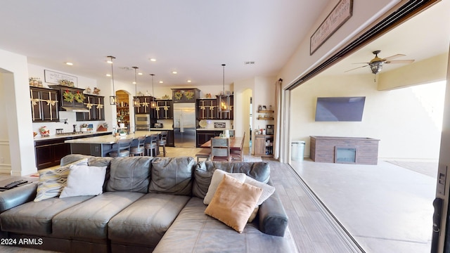 living room featuring ceiling fan with notable chandelier, light wood-type flooring, and sink