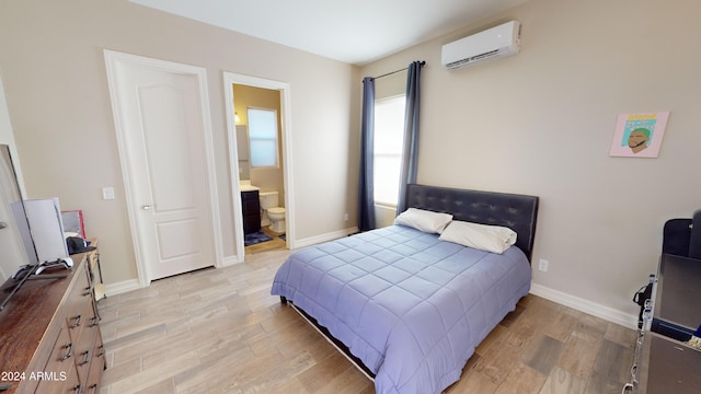 bedroom featuring connected bathroom, a wall mounted AC, and light hardwood / wood-style flooring