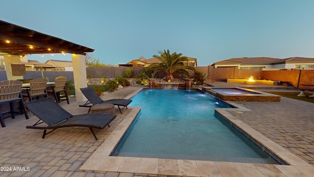 pool at dusk with pool water feature, a patio area, a pergola, and an in ground hot tub