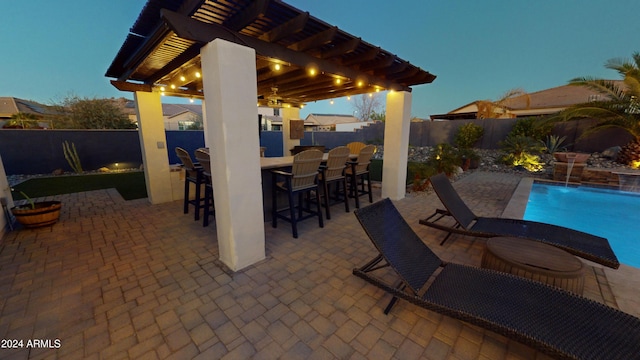 patio terrace at dusk featuring pool water feature, ceiling fan, a fenced in pool, and exterior bar