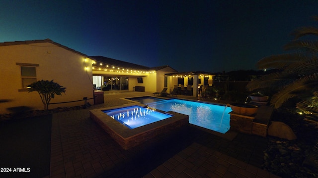 pool at twilight featuring an in ground hot tub and a patio