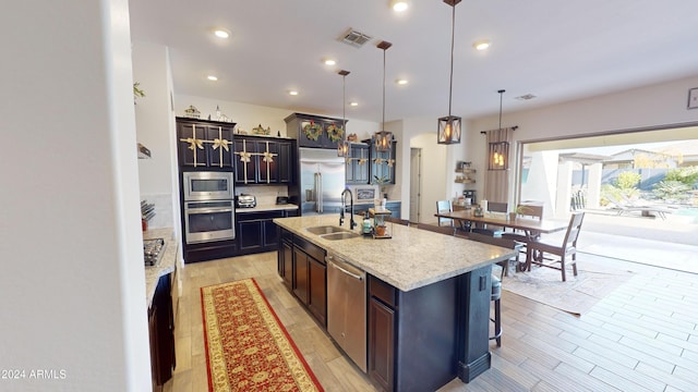 kitchen with sink, built in appliances, a center island with sink, light hardwood / wood-style floors, and hanging light fixtures