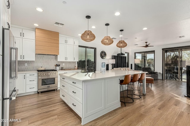 kitchen featuring custom exhaust hood, white cabinetry, appliances with stainless steel finishes, pendant lighting, and a kitchen island with sink