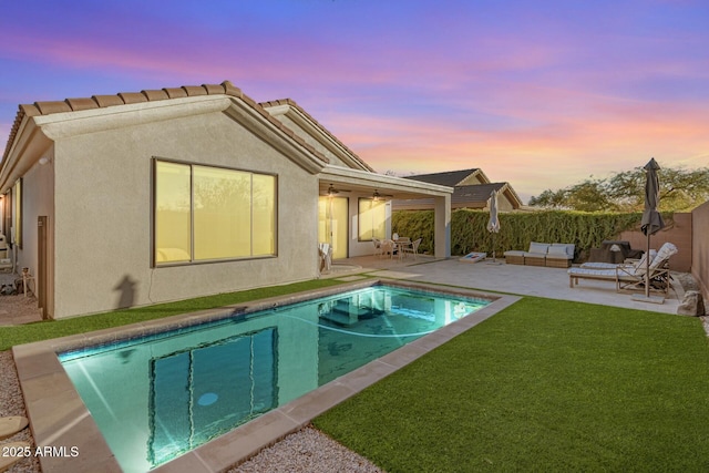 back house at dusk featuring a yard, outdoor lounge area, a fenced in pool, and a patio area