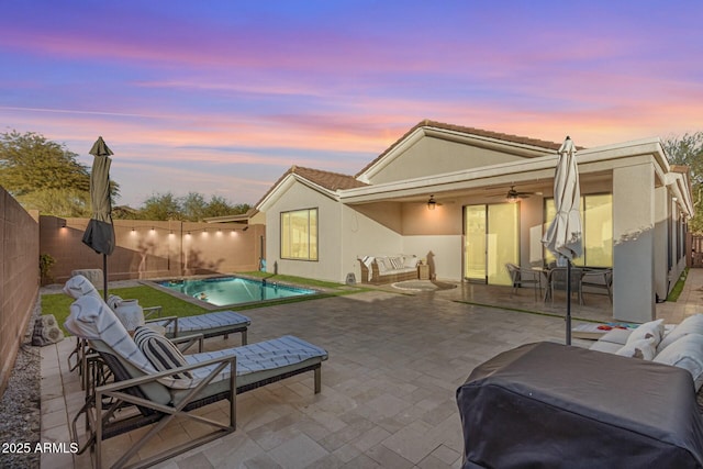 pool at dusk featuring outdoor lounge area, ceiling fan, and a patio area