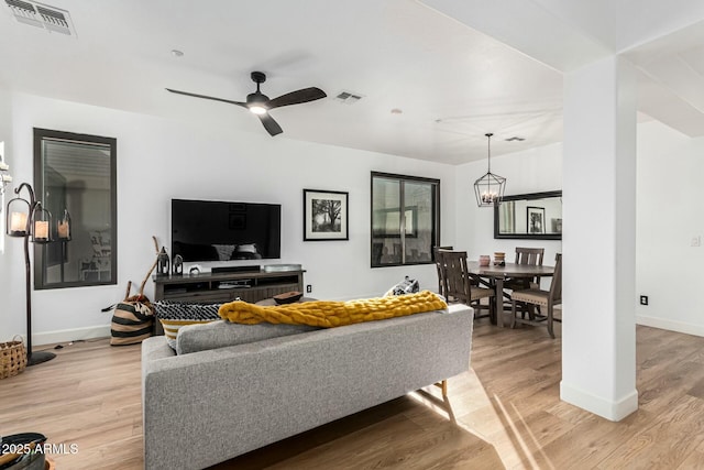 living room featuring ceiling fan with notable chandelier and light wood-type flooring