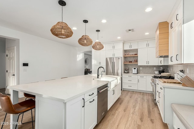 kitchen featuring an island with sink, sink, white cabinets, hanging light fixtures, and stainless steel appliances