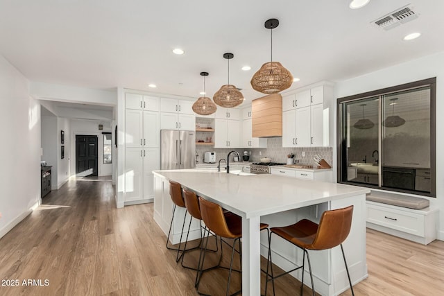 kitchen with decorative light fixtures, appliances with stainless steel finishes, white cabinets, a kitchen island with sink, and backsplash