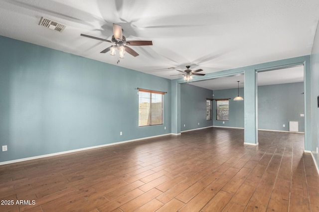 empty room with baseboards, a ceiling fan, wood finished floors, and visible vents