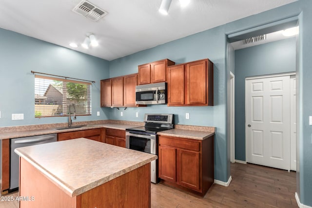 kitchen with brown cabinetry, visible vents, appliances with stainless steel finishes, a sink, and light wood finished floors