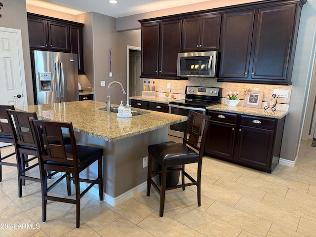 kitchen with a kitchen island with sink, a kitchen breakfast bar, sink, light stone counters, and stainless steel appliances