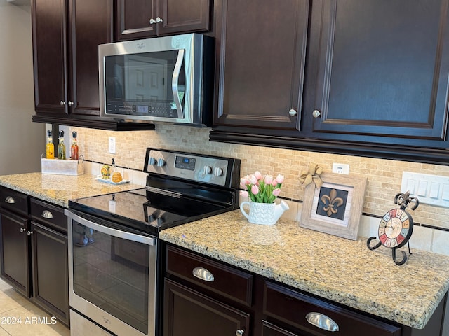 kitchen with backsplash, dark brown cabinetry, light stone countertops, and appliances with stainless steel finishes